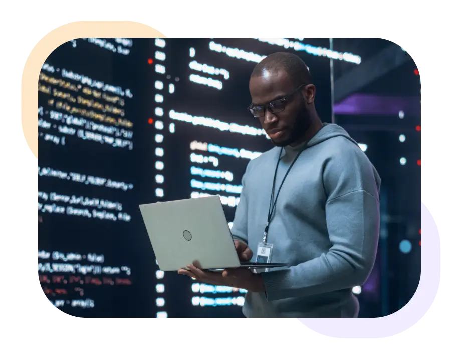 Mann mit Laptop steht vor einer Wand mit Codezeilen. 